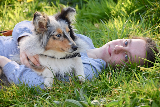 Woman laying on grass with her dog laying on top of her.
